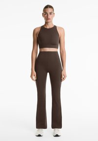 Top court ajusté marron et pantalon évasé assorti en matériau extensible, avec une texture lisse et sans logos ni motifs visibles.