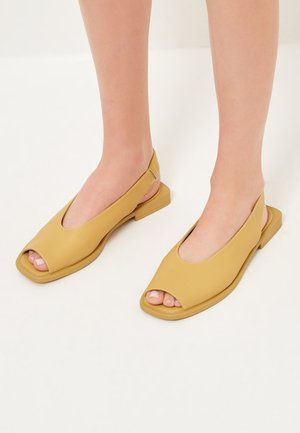 Offene Sandalen in Senfgelb, gefertigt aus glattem Leder. Verfügen über ein Slingback-Design mit flacher Sohle und minimalistischen Nähdetails.