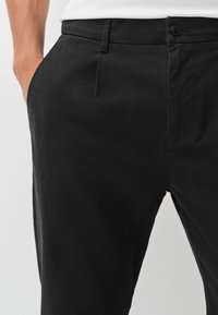 Chinos en coton noir avec une texture lisse, coupe slim, plis discrets à l'avant, poches latérales et fermeture par bouton.