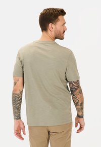 Oliven grøn kortærmet t-shirt i en afslappet pasform. Blød tekstur med rund hals og synlige syninger. Modellen har tattooer på armene.