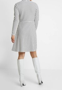 Randig klänning i svart och vitt med långa ärmar, en figursydd bodice och en utsvängd kjol. Baksidan har en hög halsringning och en slät yta.