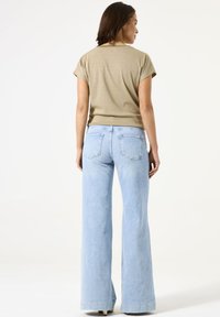 Blusa beige de manga corta con cuello redondo combinada con jeans acampanados de color azul claro que cuentan con bolsillos y una textura suave.