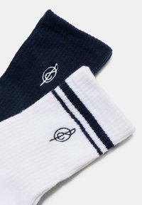 Chaussettes en mélange de coton bleu marine et blanc, avec une texture côtelée. La chaussette blanche présente des rayures bleu marine et un détail de logo subtil.