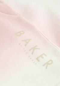 Šviesiai rožinė ir balta gradientinė medžiaga su minkštu paviršiumi. Aukso spalvos "BAKER" logotipas, esantis priekyje, modernus tipografijos dizainas.