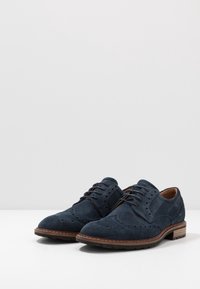 Brogues en daim bleu marine avec des détails perforés, un bout rond et des accents en cuir marron. Caractérisés par une fermeture à lacets et un talon empilé.