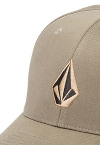 Tan kasket med en buet skygge, prydet med et broderet logo i sort og guld. Fremstillet af tekstureret stof med syninger på siderne.