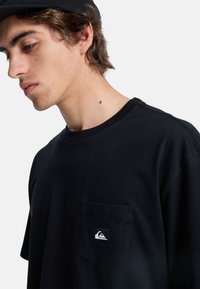 Sort bomulds T-shirt med rund hals, korte ærmer og en brystlomme med en hvid logo detalje. Glat tekstur, afslappet design.