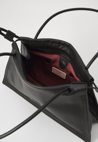 Borsa in pelle nera con ampia apertura, sottili spalline e fodera in tessuto bordeaux. Include una piccola etichetta interna e hardware minimale.