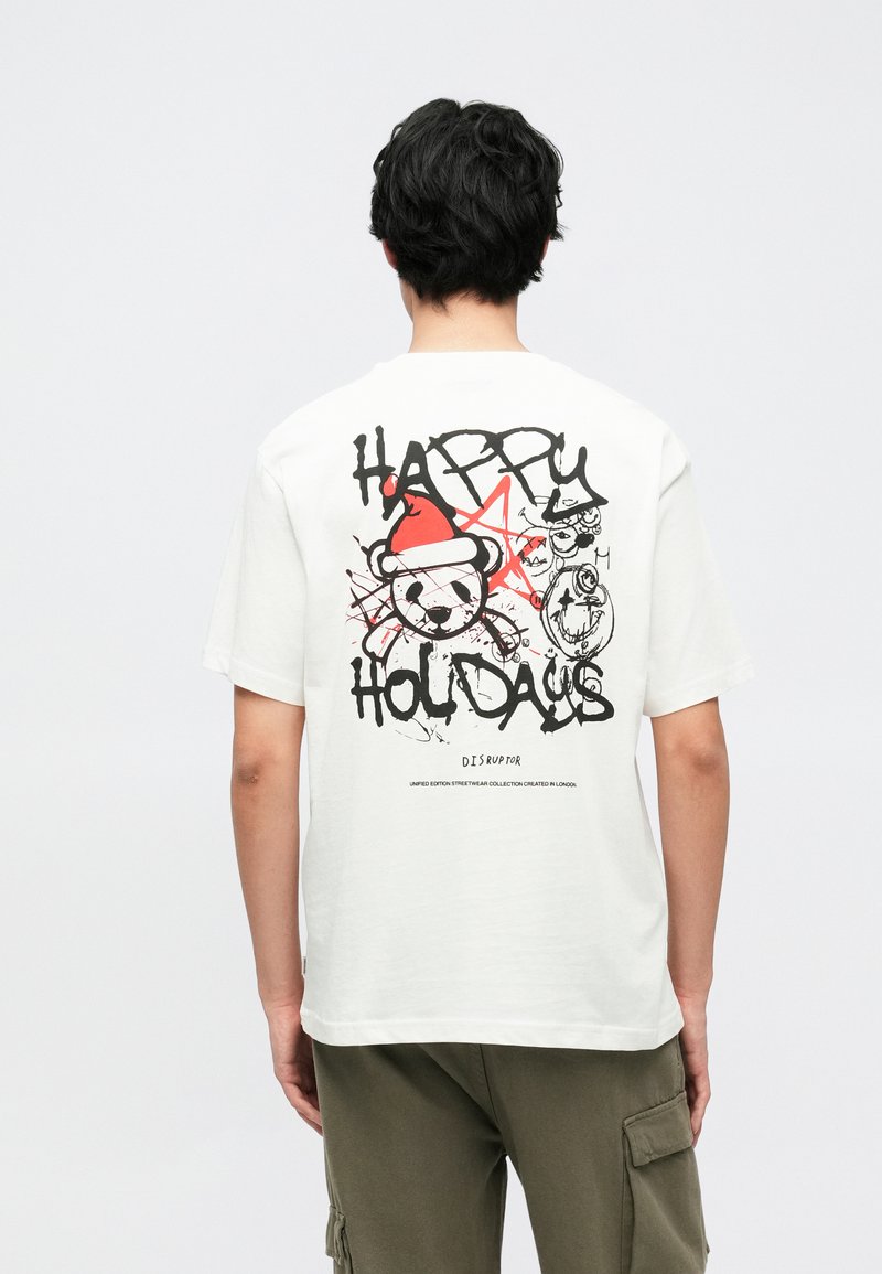 Hvid bomulds-T-shirt med sort og rød grafik på ryggen med teksten "GLÆDELIGE FERIEDAGE," stjerne-detaljer og tegneseriefigurer.