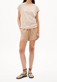 Beżowa koszulka w paski z podwiniętymi rękawami w połączeniu z beżowymi szortami. Czarne sandały z zielonymi akcentami i plecionymi paskami dopełniają całość.