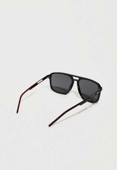 Lunettes de soleil avec des montures rectangulaires noires, des verres gris foncé et des branches avec des accents bordeaux. Fini lisse avec des détails matériels minimaux.