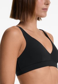 Svart bralette med V-halsdesign, tunna justerbara band och slät tyg. Har minimalistisk sömnad och en sömlös look.