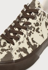 Χαμηλό sneaker με κρεμ και σκούρο καφέ μοτίβο αγελάδας, καφέ κορδόνια και σκούρα καφέ λαστιχένια σόλα.