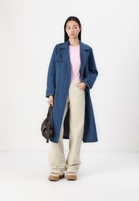 Denim plašč v temno modri barvi, z dvojno zadrgo. Nosen preko svetlo roza bluze in širokih kremnih hlač. Vključena rjava torbica in masivne čevlje.