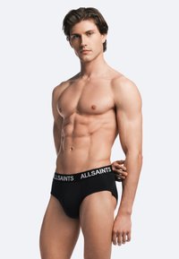 Black cotton briefs with an elastic waistband featuring "ALLSAINTS" in white. Smooth texture and fitted design, accentuating the body.