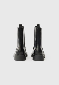 Crne kožne čizme do gležnja s glatkom površinom, s petljama za povlačenje na vrhu, detalji prošivenog dizajna i debelim gumenim potplatom.