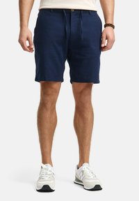 Navy blue shorts made of lightweight fabric with a drawstring waist, side pockets, and rolled hems, paired with white sneakers.