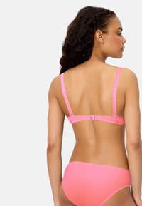 Mujer con el cabello rizado que lleva un conjunto de bikini rosa a juego, vista desde atrás contra un fondo blanco liso.