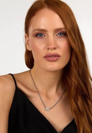 Collana d'argento con un pendente testurizzato su una catena intrecciata, indossata su una maglia nera. Il pendente presenta un design inciso.