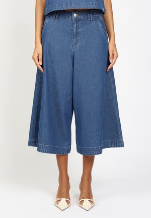 Wide-leg blue denim culottes worn with matching crop top and white pointed-toe heels on a standing model.