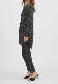 Svart blommig blus med långa ärmar, v-ringning och avslappnad passform, tillsammans med högmidjade svarta jeans och svarta öppna klacksandaler.