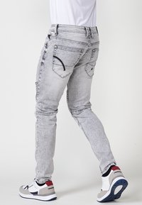 Slank-fittede, lyse grå denimjeans med slidte detaljer, fem lommer og kontrastomslag. Båret med sporty sneakers.
