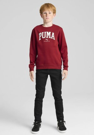 Sudadera burdeos con el logo "PUMA" en blanco. Vaqueros negros ajustados, zapatillas negras. Tejido suave, escote redondo, mangas largas, diseño minimalista.