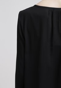 Zwarte blouse met een gladde textuur, met een ontspannen pasvorm, ronde halslijn en subtiele plooien aan de achterkant voor een designdetail.