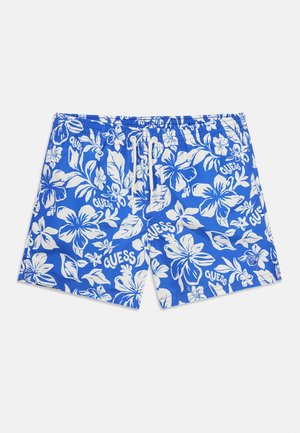 Costume da bagno blu con fiori tropicali di ibisco bianchi e loghi "GUESS", con vita elastica e coulisse bianca.