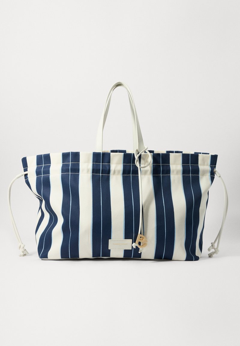 Pruhovaná taška cez rameno v námorníckej modrej a bielej plátne, so šnúrkovým uzáverom, dvojitými uchami a zlatým akcentovým štítkom. Odolný a priestranný dizajn.