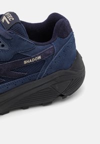 Blue suede and mesh sneaker featuring a textured rubber sole, with "SHADOW" branding on the side. Padded collar for comfort.
