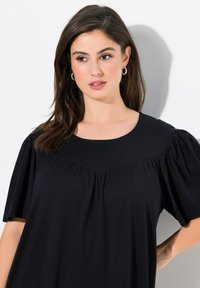 Robe noire à manches courtes avec un col rond, présentant un corsage texturé et des manches froncées. Tissu lisse avec une coupe ample.