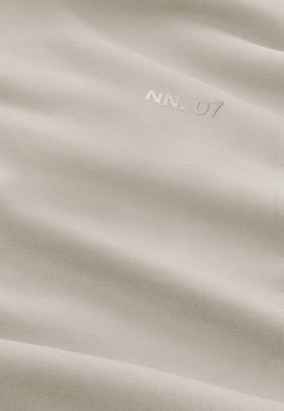 Helles beige Gewebe mit einer glatten Textur, das subtile Linien und den eingeprägten Text "NN. 07" in einem kontrastierenden Farbton aufweist.