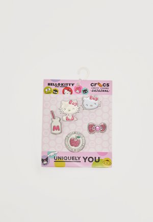 Charms Crocs Jibbitz s motívom Hello Kitty zobrazujúce tváre Hello Kitty, fľašu mlieka, ružovú mašľu a trblietavý prívesok v tvare jablka na ružovom obale.