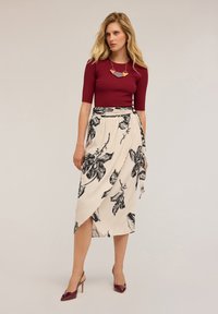 Hedvábný vínově červený top s plastickým vzorem, doplněný krémovou zavinovací sukní s černými květinovými potisky. Hladký materiál, asymetrický lem, obuté s burgundskými lodičkami.