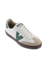 Basket blanche avec des accents verts et un bout en suède beige. Elle présente des lacets blancs et une semelle en caoutchouc, mettant en avant un design sportif mais décontracté.