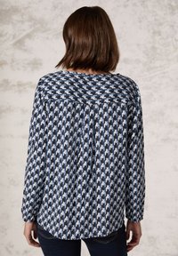 Haut à manches longues avec un motif pied de poule en marine et bleu clair. Fabriqué en tissu doux, avec une coupe décontractée et un col rond.