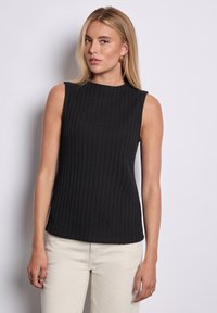 Sort ærmeløs top lavet af ribbet stof, med en høj halsudskæring og tætsiddende silhuet. Båret med lyse bukser.