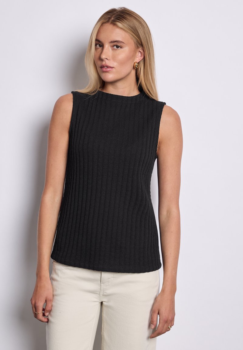 Sort ærmeløs top lavet af ribbet stof, med en høj halsudskæring og tætsiddende silhuet. Båret med lyse bukser.