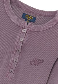 Paarse geribbelde langslaventop met een knoopsluiting bij de henley-halslijn, met een borduursel van een hart en pijl op de borst en een textuurstof.