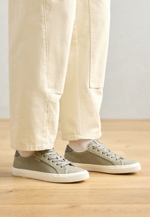 Lysgrønne lærredssneakers med grå detaljer, flade snørebånd og en tekstureret gummisål, parret med lysecreme farvede løse bukser.