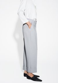 Hellgraue, maßgeschneiderte Hose mit geradem Schnitt, ausgestattet mit seitlichen Taschen und aufgeschlagenen Säumen. Kombiniert mit schwarzen, spitzen Ballerinas.