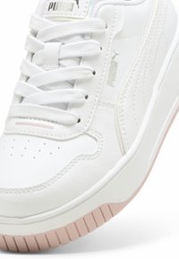 Baskets en simili cuir blanc avec bout rond, surface texturée, plusieurs trous pour les lacets et une semelle en caoutchouc rose. Détail du logo Puma en argent.