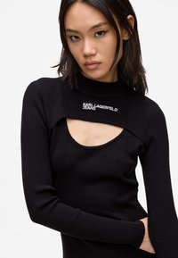 Melnas ribotas garām piedurknēm blūze ar unikālu izgriezumu un augstu apkakli. "Karl Lagerfeld Jeans" logo izšūts ap kaklu.