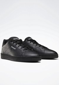 Black Reebok sneakers made of leather with a smooth texture, featuring round toes, flat black soles, and contrasting logo on the side.