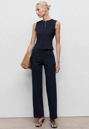 Ensemble deux pièces bleu marine avec un top sans manches en peplum et un pantalon à jambes larges, fabriqué en tissu texturé. Accessoirisé avec un sac à main beige.