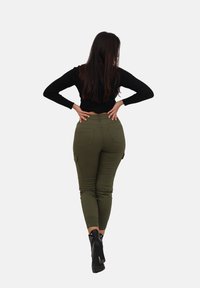 Oliwkowe spodnie typu cargo o dopasowanym kroju, z przednimi i tylnymi kieszeniami, w zestawieniu z czarnym, prążkowanym, długim rękawem oraz czarnymi botkami na wysokim obcasie.