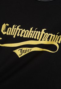 Zwarte t-shirt met grote gele gotische tekst die "Califreakinfernía Juicy" over de voorkant weergeeft, met een soepele stofstructuur.