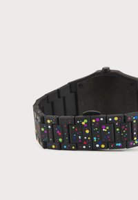 Montre noire avec un bracelet en silicone coloré et moucheté, présentant des points de tailles variées en rose, bleu, vert et jaune sur ses maillons.