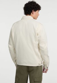 Cremfarbene Jeansjacke mit Kragen, langen Ärmeln und geknöpften Manschetten. Verfügt über seitliche Taschen und einen geraden Saum.